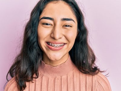 Hispanic teenager girl with dental braces showing orthodontic brackets looking positive and happy standing and smiling with a confident smile showing teeth