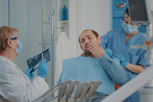 Patient complaining about toothache at stomatology consultation while dentist analyzes dental radiography to do drill procedure. Senior stomatologist treating caries for oral care.